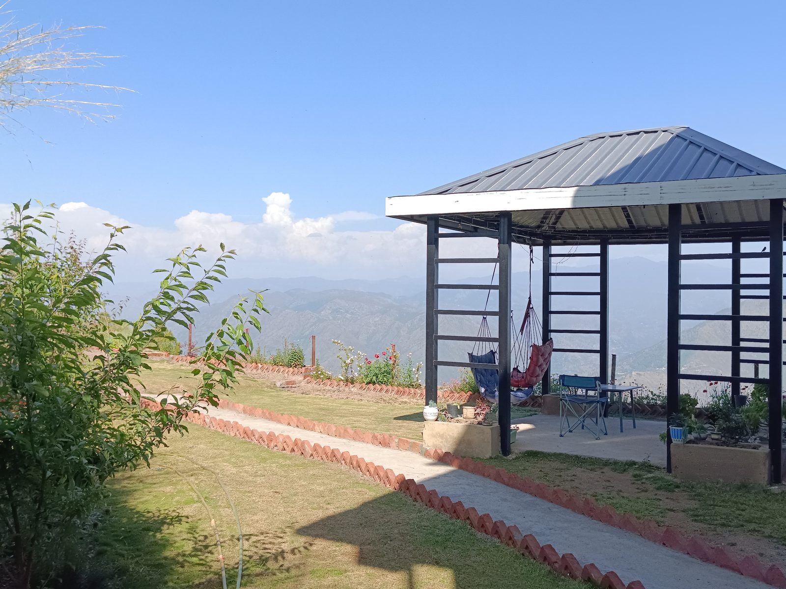 Gazebo with hanging seats and mountain range in the distance on a clear summer day