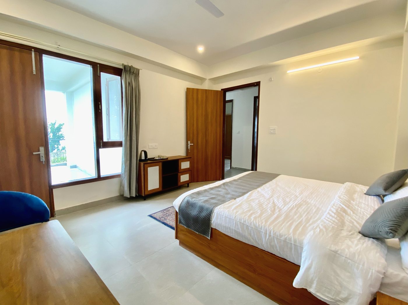 Room in natural daylight with a king bed, balcony access and a wooden side chest