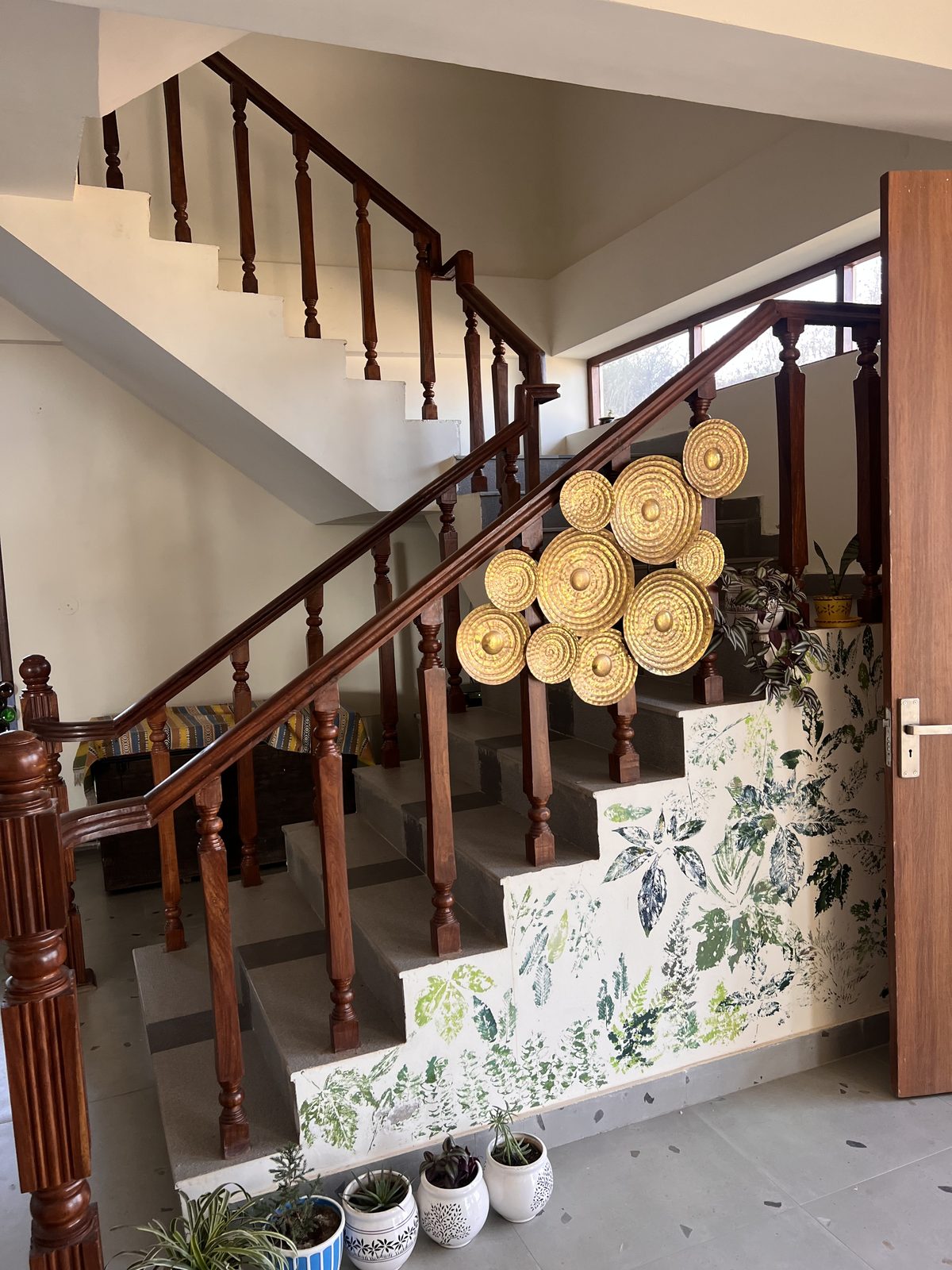 Wooden stairwell with turned balusters, a cluster of brass sun-medallions and botanical prints on the wall