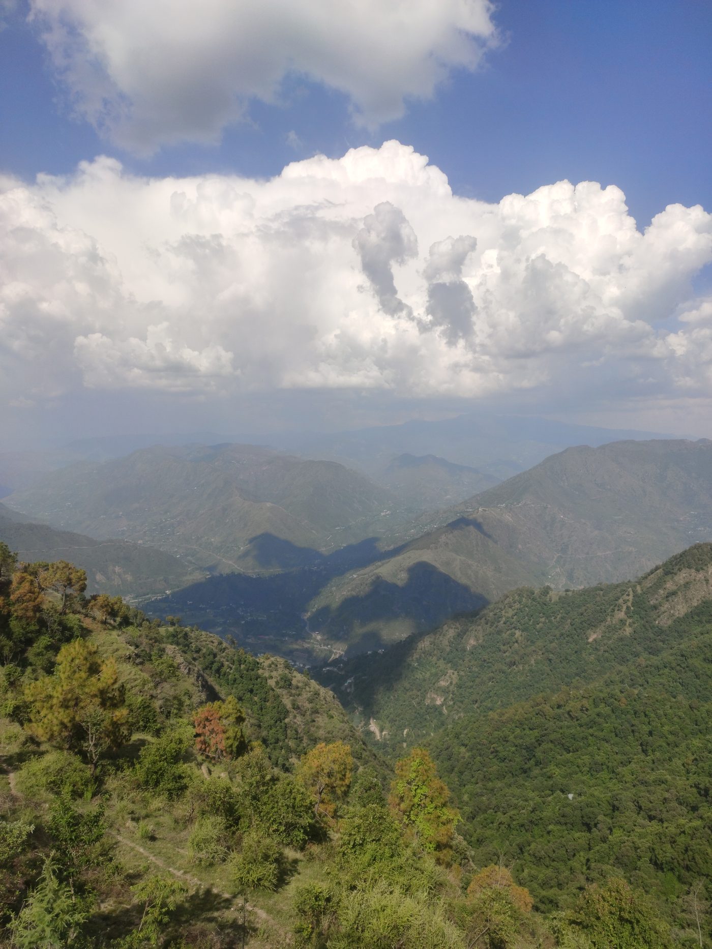 Summer cloudscape over the Himachal foothills — cumulus clouds piled over layered green ridges