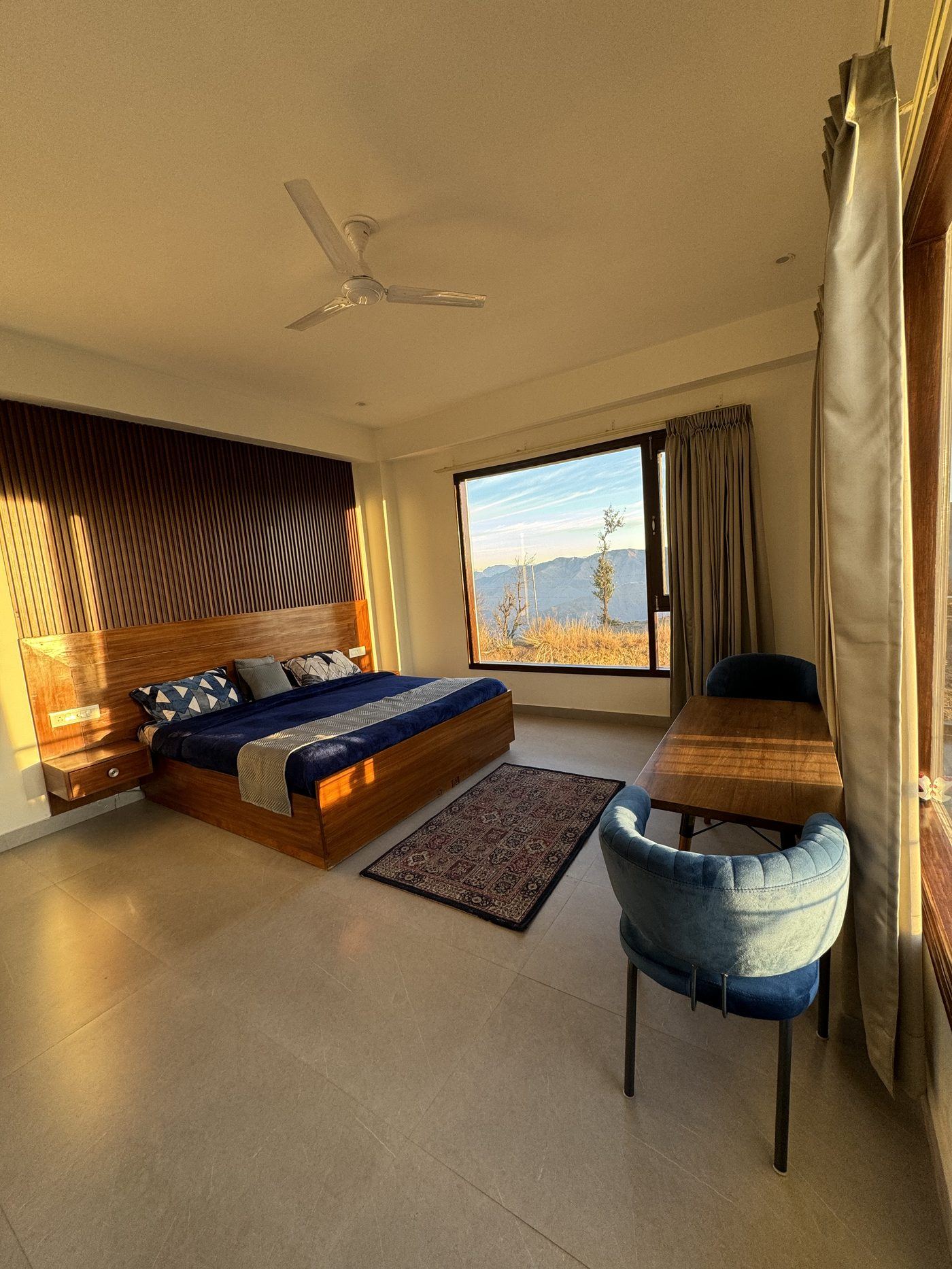 Super Deluxe room at golden hour — king bed, warm wood panelling and the mountain view through a large window